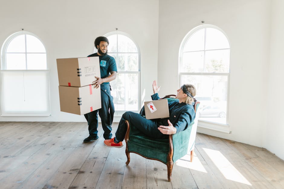 A professional removal service technician from Man and Van Earls Court is shown indoors during a home relocation process, lifting two cardboard boxes with red and black labels. The technician, dressed
