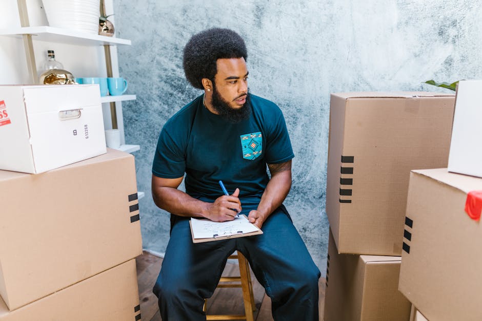 A professional removal service technician from Man and Van Earls Court is shown indoors during a home relocation process, lifting two cardboard boxes with red and black labels. The technician, dressed